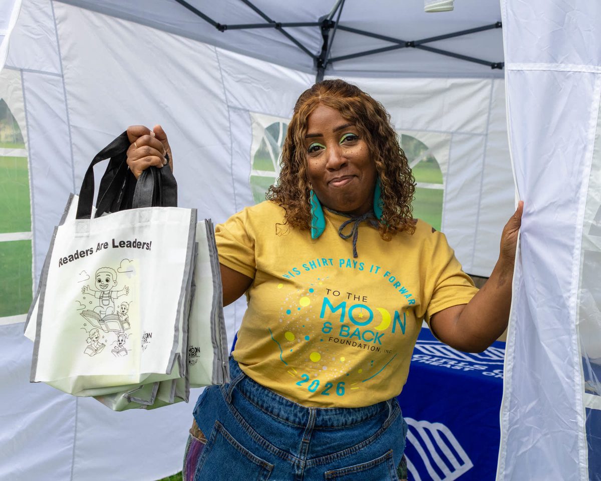 Volunteer holding up a tote bag under the tent
