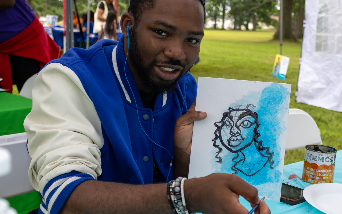 Young man in a blue jacket smiling and holding up his finished portrait, photographed by JS Media